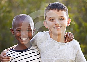 Two boys, arms around each other smiling to camera outdoors