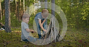 Two boys brothers 3-6 years old in the forest collect and set up campfire sticks at sunset during a family camping trip