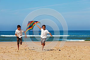 Two boys brothers run on the beach with kite