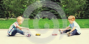 Two boys children playing together with toys cars in the park on summer day