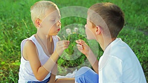 Two boys dressed in white, blowing dandelions on