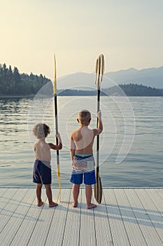 Two boys on the edge of the dock of a beautiful scenic lake during their summer vacation. Ready to paddle in the water