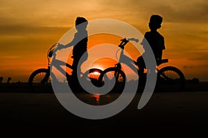 two boys enjoying the sunset on a bicycle