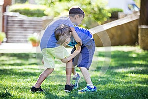 Two boys fighting outdoors. Siblings or friends wrestling on grass in summer park