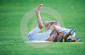 Two boys fighting outdoors. Siblings wrestling on grass in park