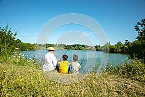 Two boys with fishing rods catch fish on the pond with a grandfather