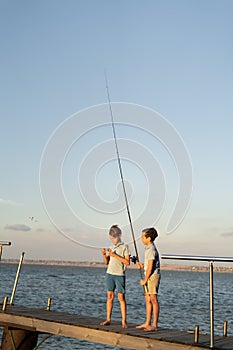 Two boys is fishing at sunset on the lake. Kids are playing on nature with fishing rod.