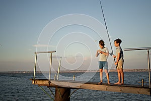 Two boys is fishing at sunset on the lake. Kids are playing on nature with fishing rod.