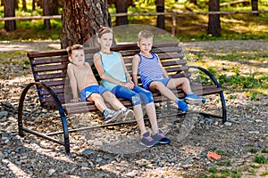 Two boys and a girl sitting on a bench in the summer. Three children