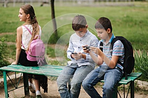 Two boys and girl use their phones during school breack. Cute boys sitting on the bench and play online games