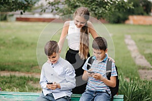 Two boys and girl use their phones during school breack. Cute boys sitting on the bench and play online games