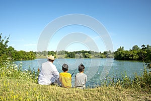 Two boys and grandfather are fishing on  a pond.  They are surrounded by beautiful nature.  Fishing is a dream for children