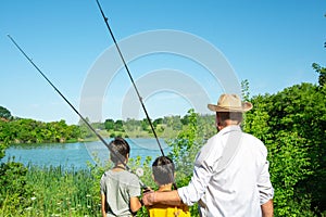 Two boys and grandfathers went fishing.  They stand on the shore of the pond and look into the distance