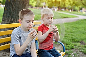 Two boys have a snack on a bench in the park and chat. Summer day