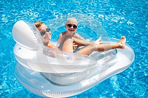 Two boys having fun playing on a floating mattress in a swimming