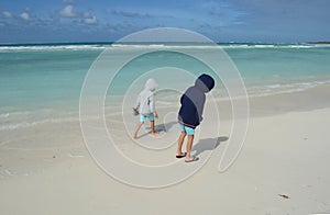 Two boys in hoodies walking on white sand of a tropical beach