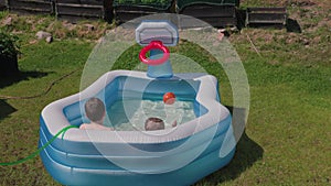 Two boys in inflatable outdoor swimming pool playing water basketball on backyard on sunny summer day.
