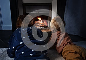 Two boys lay in front of the home fireplace look at fire