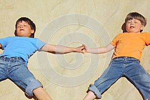 Two boys lie on sand with closed eyes