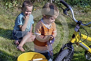 Two boys.Little boy washes their bike outdoors.