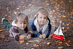 Two boys, lying on the ground, playing with a boat