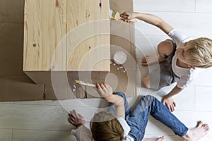 Two boys painting wooden curbstone with brush. Children renovating table. Top view