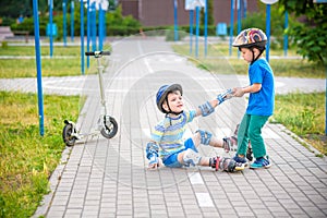 Two boys in park, help boy with roller skates to stand up