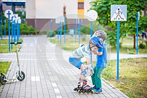 Two boys in park, help boy with roller skates to stand up