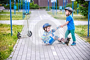 Two boys in park, help boy with roller skates to stand up