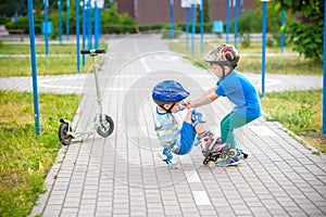 Two boys in park, help boy with roller skates to stand up