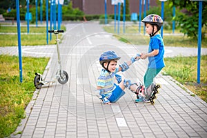 Two boys in park, help boy with roller skates to stand up