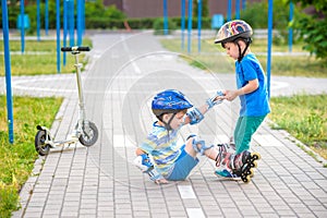 Two boys in park, help boy with roller skates to stand up