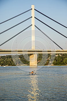 Two boys peddling kayak on Danube river near bridge