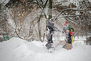 Two boys play on a pile of snow after heavy snowfall in the city. Children on a walk in the park in winter. Active healthy