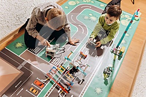 Two boys play with robots that they created from the robotic constructor on the colorful banner on the floor in the