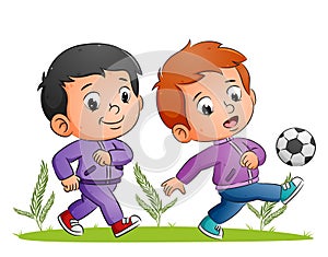 The two boys are playing the football and kicking the ball in the field