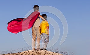 Two boys playing superheroes on the sky background, Superhero protects younger friend