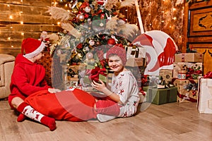 Two boys in red clothes open gifts sitting under the Christmas tree