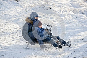 Two boys ride on sleds, descend from a snowy mountain and brake with their feet