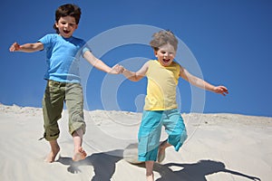 Two boys run on sand