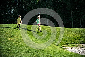 Two boys are running through the golf filed hills on the green grass and forest on background