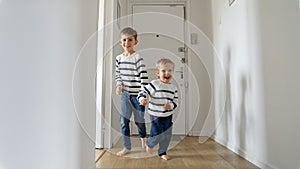 Two boys a running with smiles on their faces on a wooden floor in a long corridor at home. This footage is perfect for