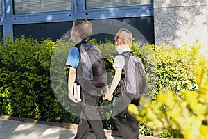 Two boys, schoolchildren in black school uniforms with backpacks go to school, hold hands, friendship concept, friendly sibling,