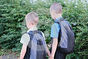 Two boys, schoolchildren in black school uniforms with backpacks go to school, hold hands, friendship concept, friendly sibling,