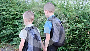 Two boys, schoolchildren in black school uniforms with backpacks go to school, hold hands, friendship concept, friendly sibling,