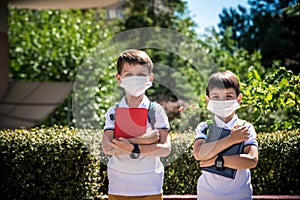 Two boys, schoolchildren in black school uniforms with backpacks in a medical mask go to school independently, hold hands,