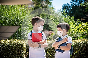 Two boys, schoolchildren in black school uniforms with backpacks in a medical mask go to school independently, hold hands,