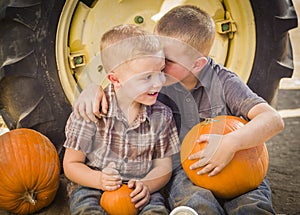 Two Boys Sitting Against Tractor Tire Holding Pumpkins Whispering Secrets