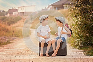 Two boys, sitting on a big old vintage suitcase, playing with to