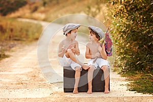Two boys, sitting on a big old vintage suitcase, playing with to